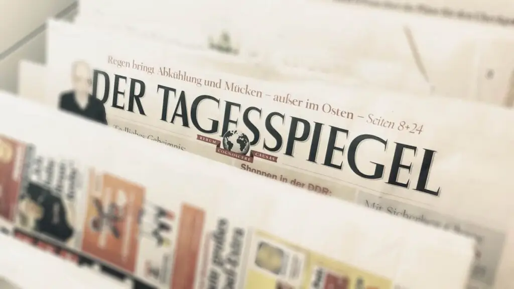 Zeitung Der Tagesspiegel im Fokus, mit Überschrift über Regen und Abkühlung. Hintergrund zeigt weitere Zeitungen.