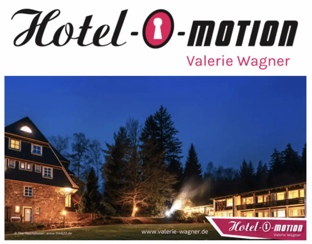 ALT-Text: Außenansicht des Hotels bei Dämmerung, umgeben von Bäumen, mit beleuchtetem Eingangsbereich und Fenstern.
