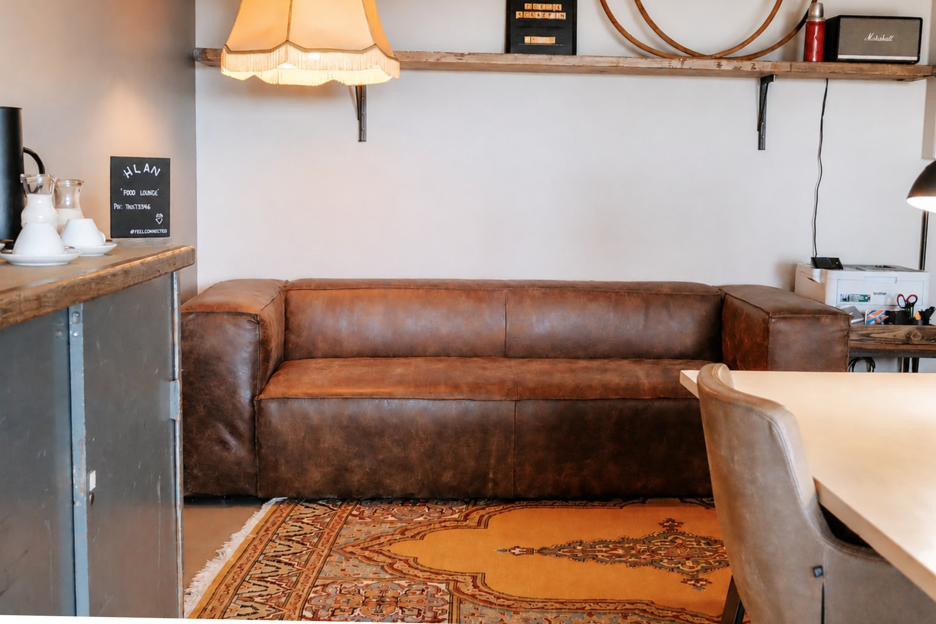Gemütliche Lounge mit braunem Ledersofa, Teppich und schlichtem Holzregal, dekoriert mit einer Lampe und Geschirr.